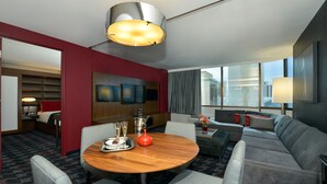 Ein Hotelzimmer mit Essbereich, einer Couch und einem großen Fenster mit Blick auf die Stadt.