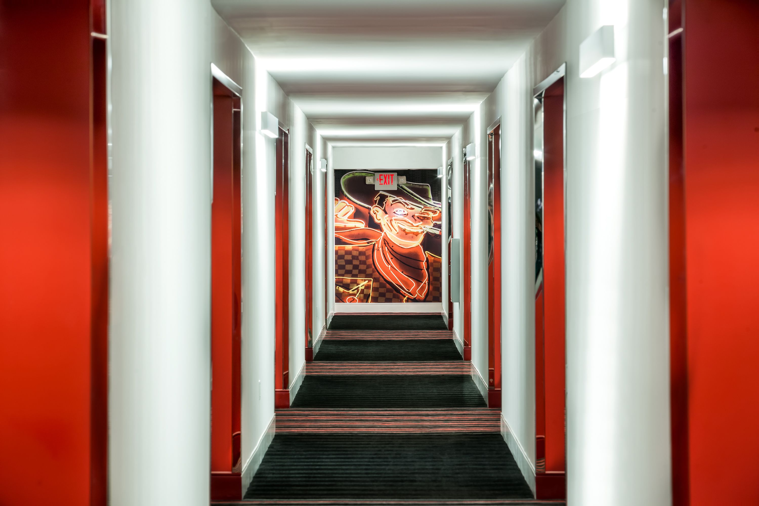 Un pasillo con una decoración roja y blanca, un letrero de salida neón y un patrón de suelo a cuadros.
