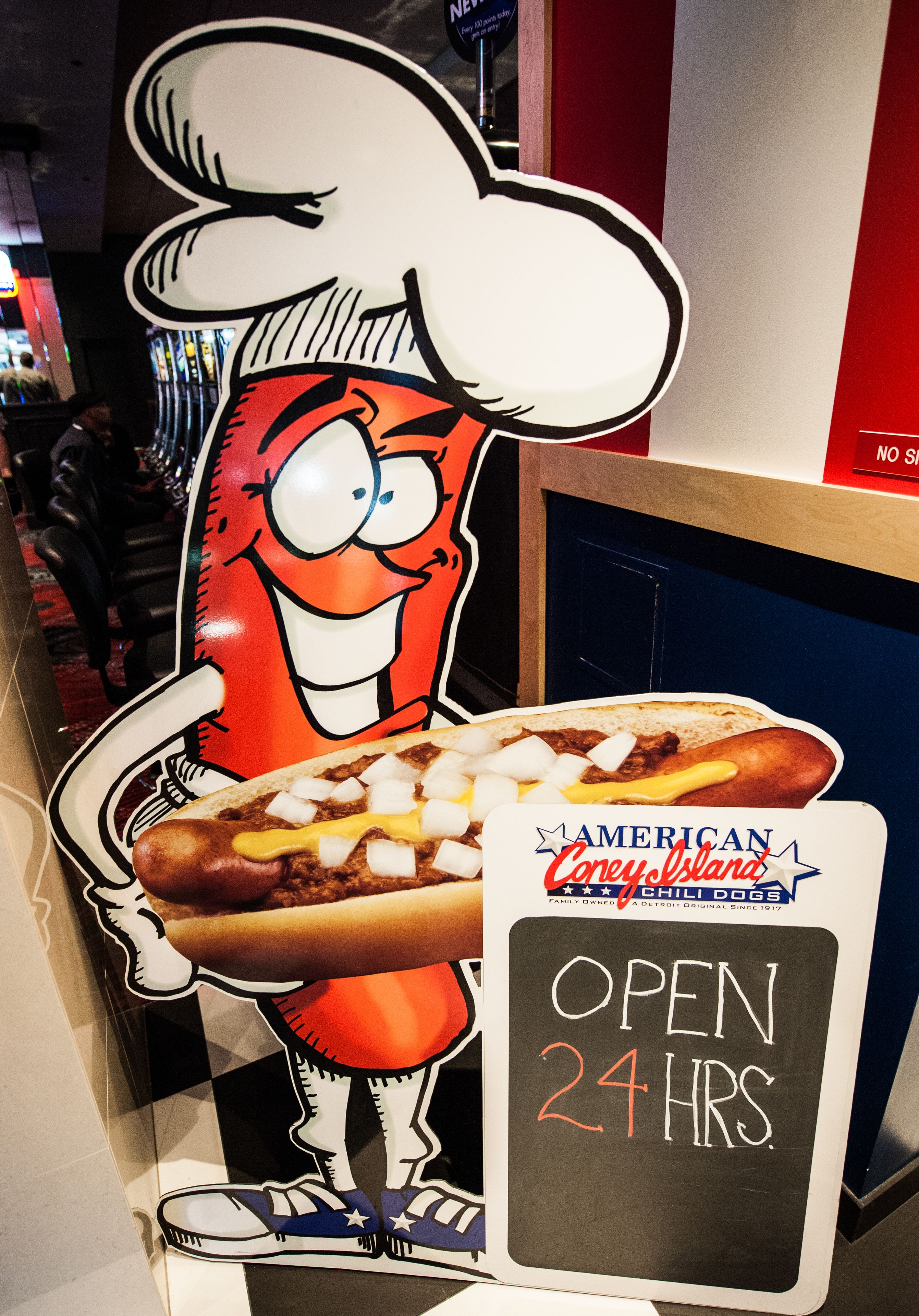 Un personnage de dessin animé tenant un hot-dog garni, et une pancarte indiquant « American Corey Island Chili Dogs » et « OUVERT 24 HEURES ».
