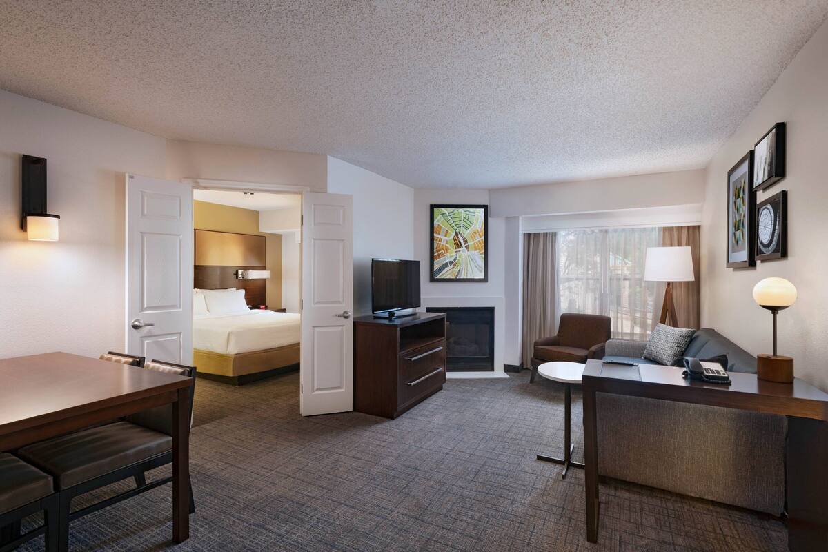 A hotel room with a bed, a desk, a chair, a TV, a fireplace, and a window with curtains.