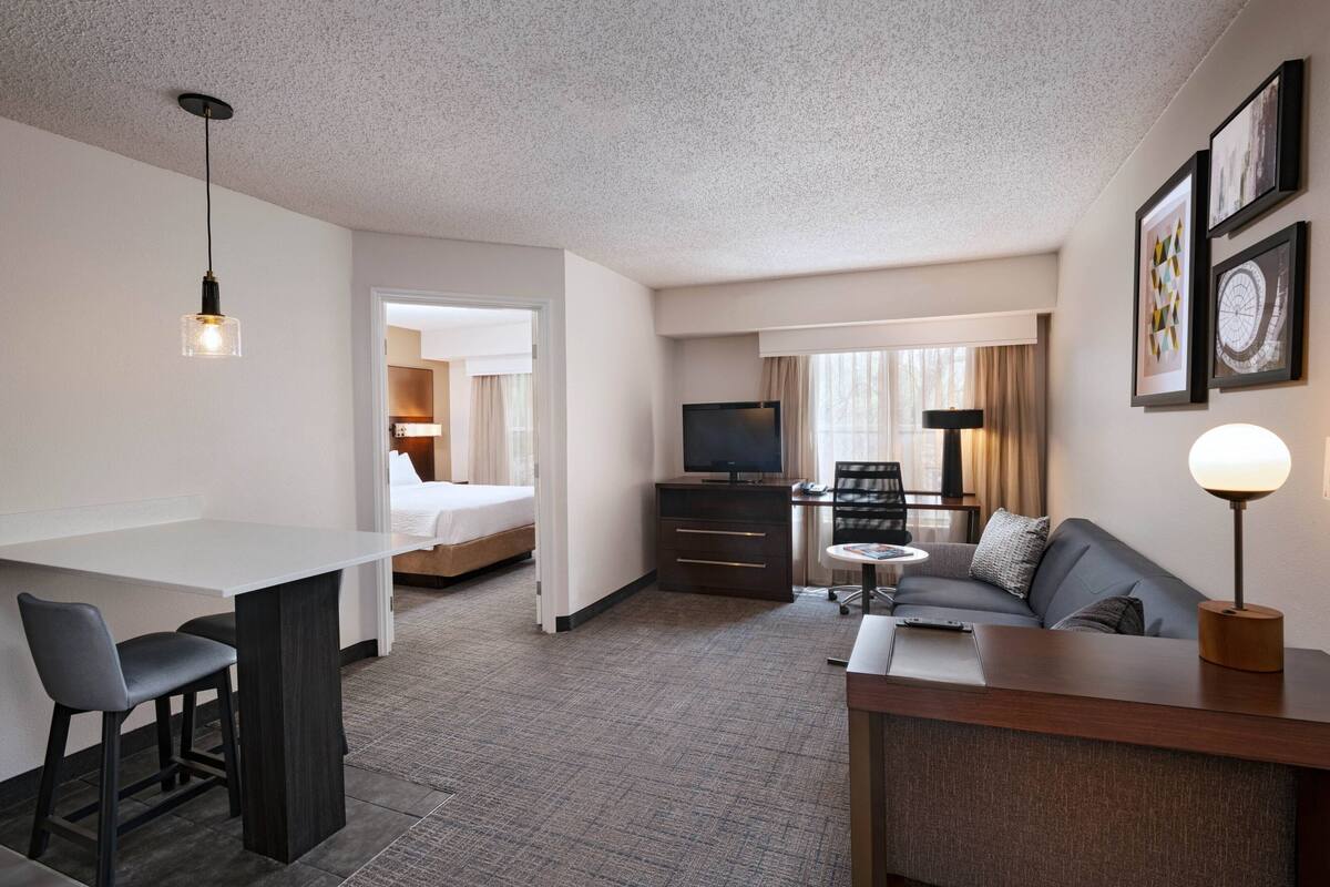 A hotel room with a bed, a desk with two chairs, a sofa, a TV, and a lamp.
