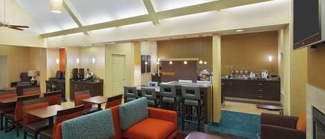 Un vestíbulo de hotel con comedor, cocina y asientos, y un ventilador de techo.