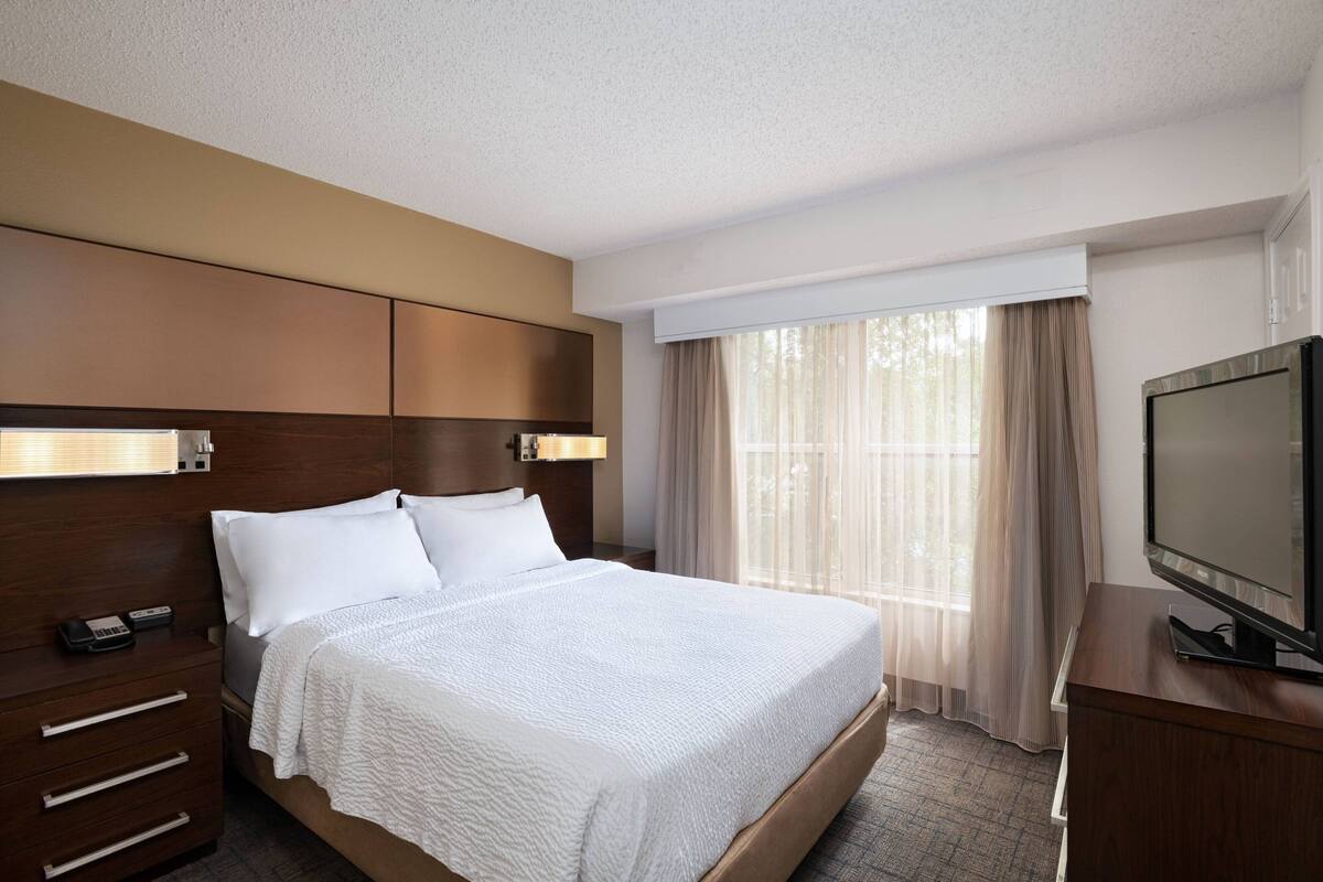 A hotel room with a large bed, a TV, a desk, and a window with curtains.