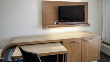 A hotel room with a wooden desk, a flat-screen TV mounted above it, and a chair.
