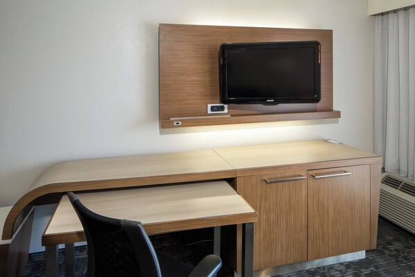 A hotel room with a wooden desk, a flat-screen TV mounted above it, and a chair.