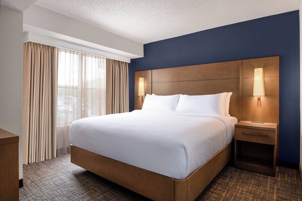 A hotel room with a large bed, a nightstand, a lamp, and a window with curtains.