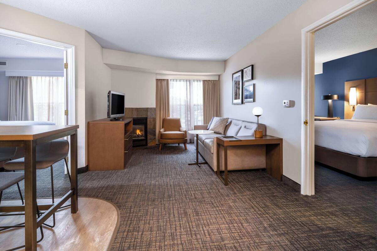 A hotel room with a bed, a desk, a sofa, a TV, and a fireplace.