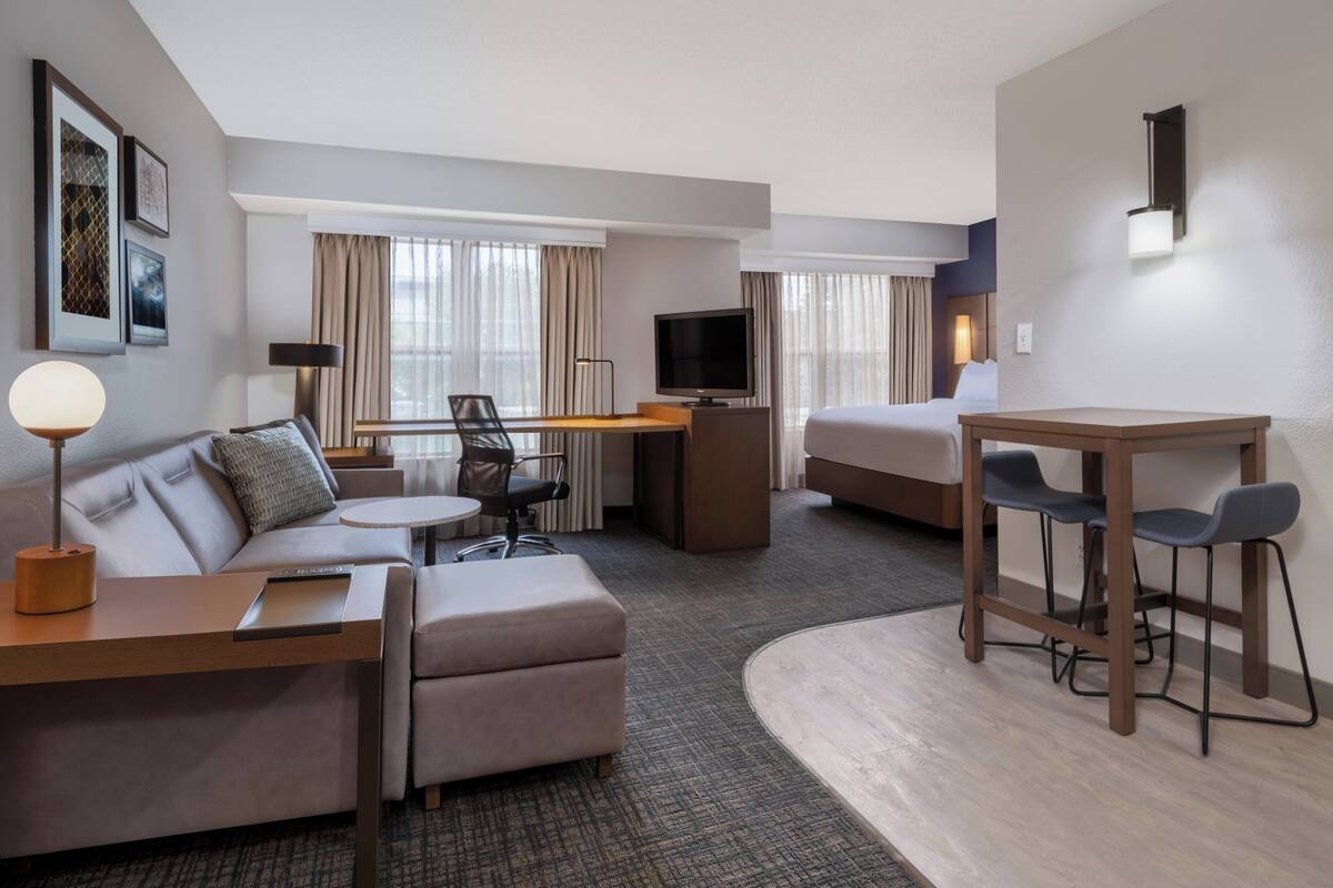 A hotel room with a sofa, a desk, a TV, a bed, and a small table with chairs.