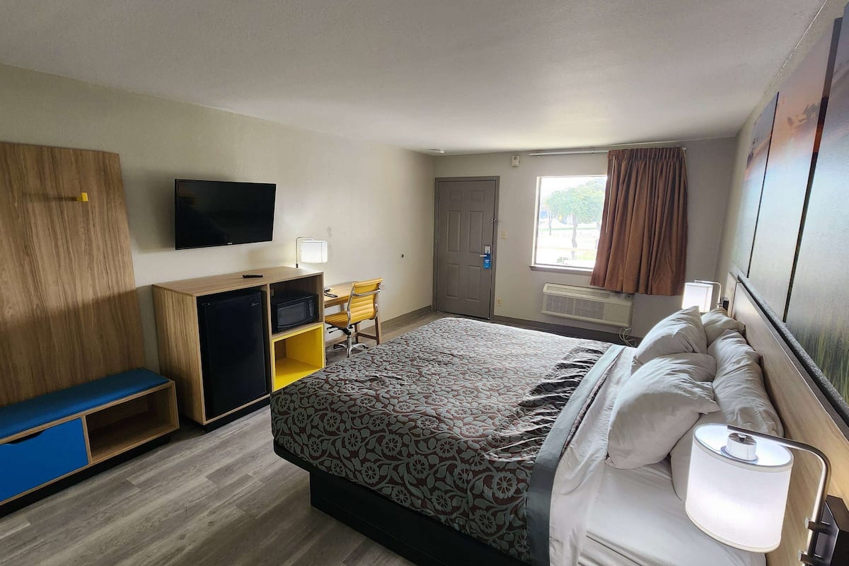 A hotel room with a bed, a desk, a television, and a window with curtains.