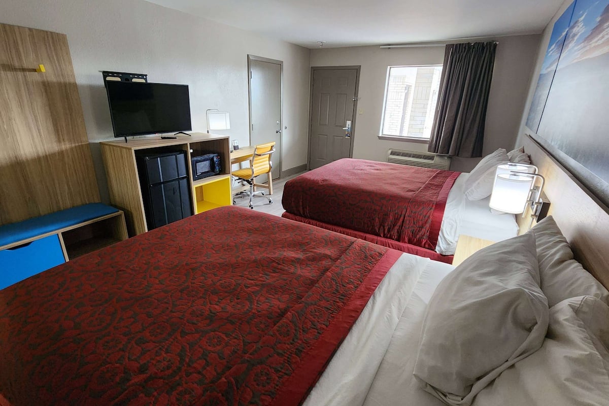A hotel room with two beds, a desk with a chair, a television, and a window with curtains.