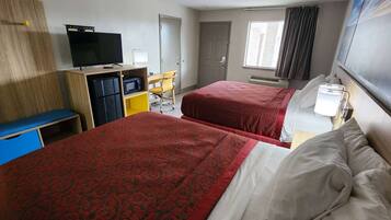 A hotel room with two beds, a desk with a chair, a television, and a window with curtains.