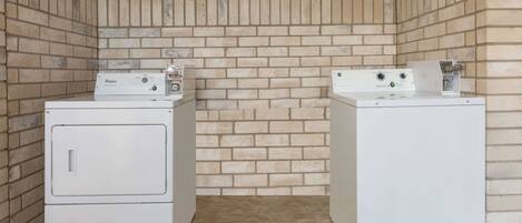 Two stacked washer and dryer units in a laundry room with a brick wall background.