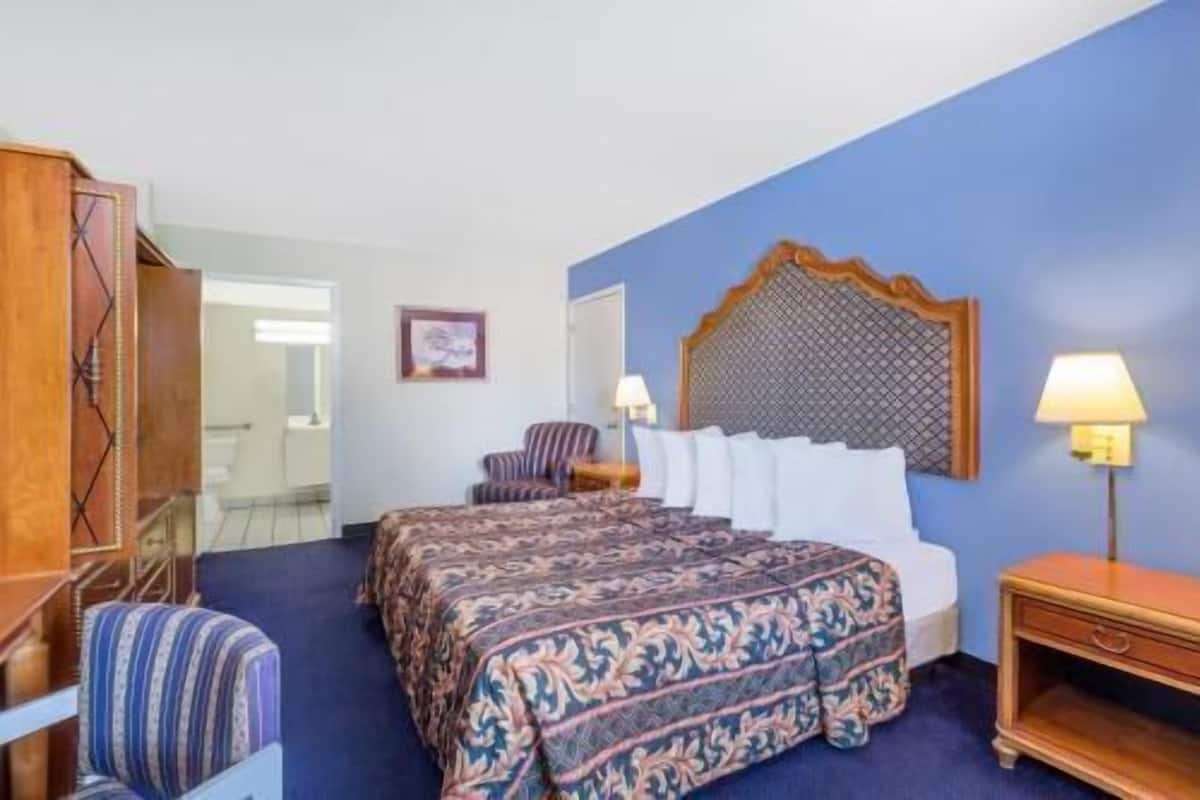 A hotel room with a bed, a chair, a nightstand, and a lamp.