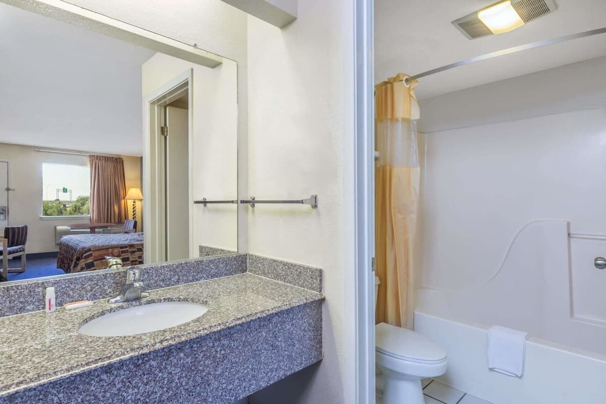 A hotel bathroom with a granite countertop sink, a mirror, a shower with a curtain, and a toilet.
