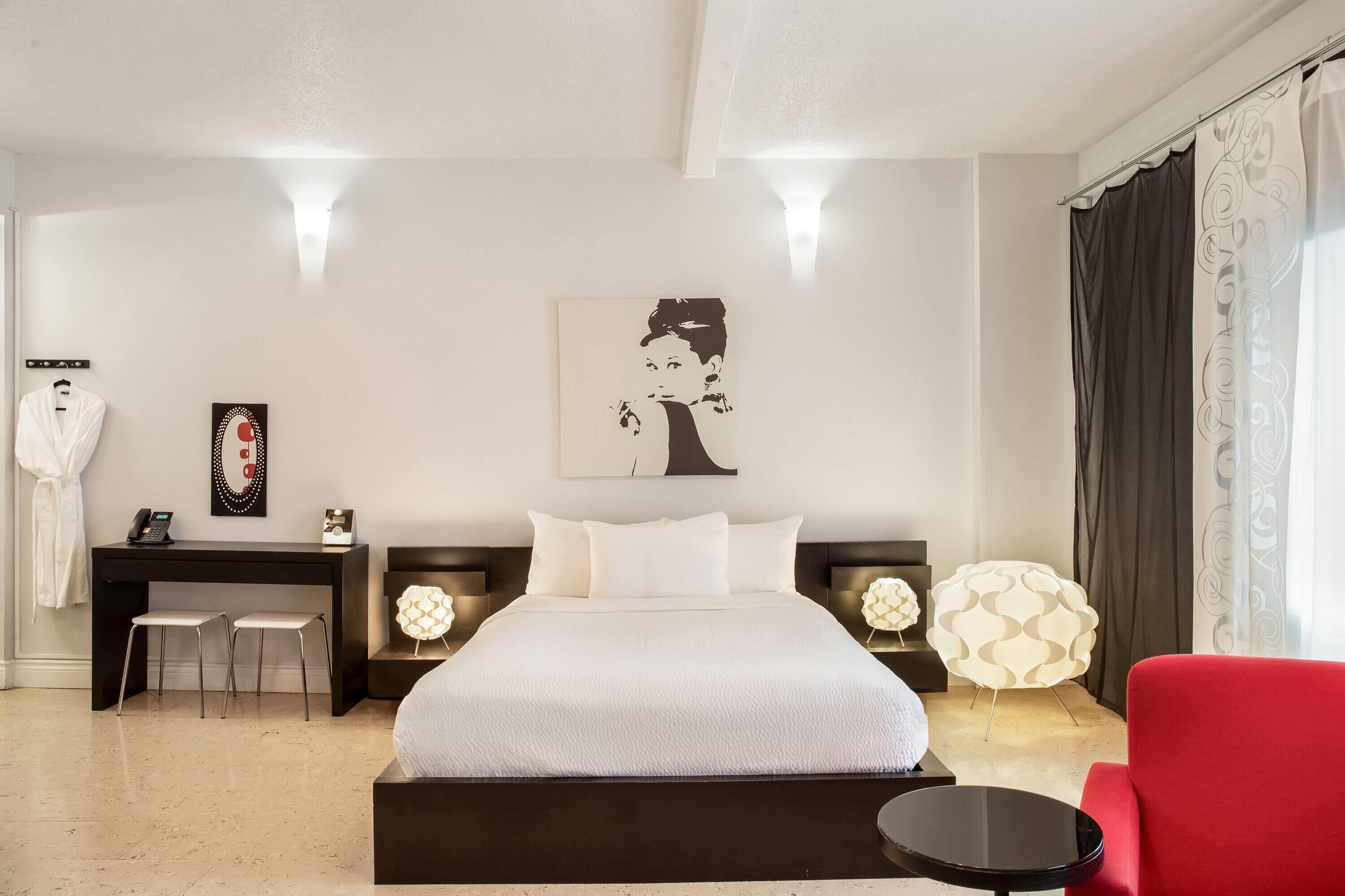 Una habitación de hotel moderna con una cama grande, un escritorio con dos sillas, un sillón rojo y decoración en la pared.