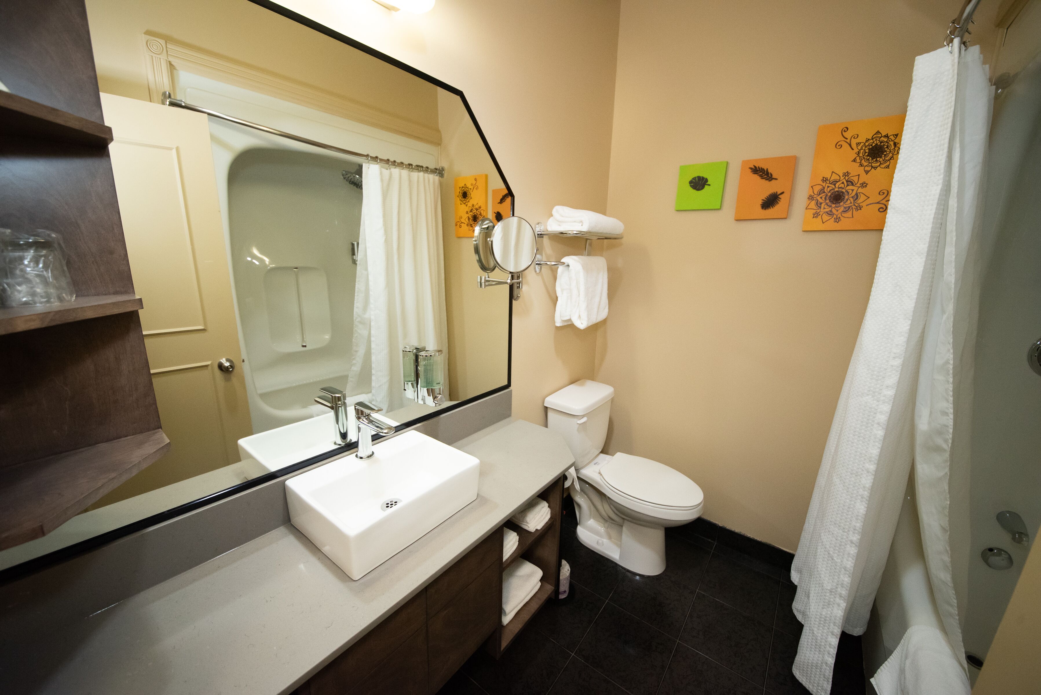 A bathroom with a white sink, toilet, and shower. There are towels and a mirror.