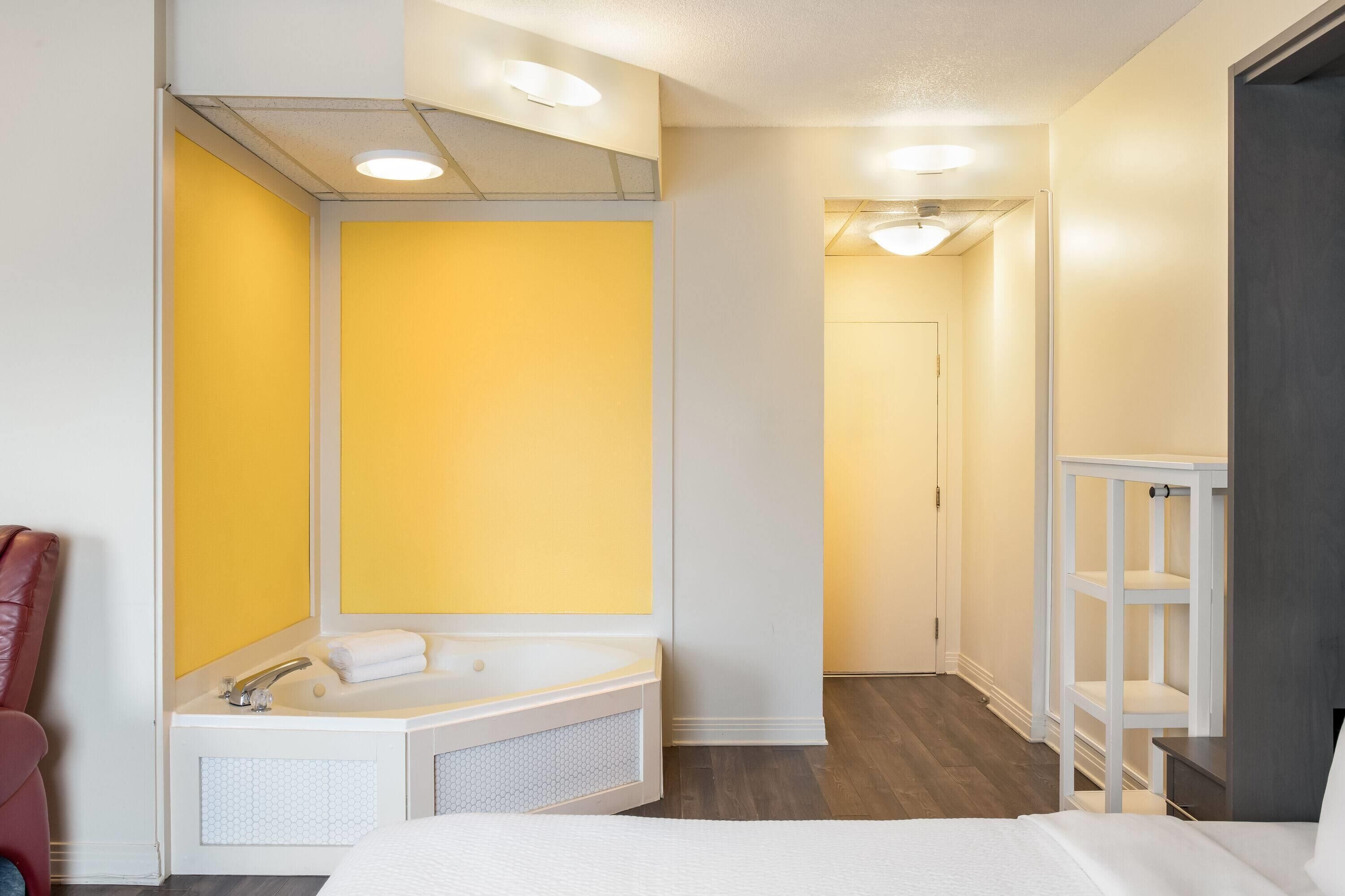 Een hotelkamer met een groot bad, een wit bed en een gele accentmuur.