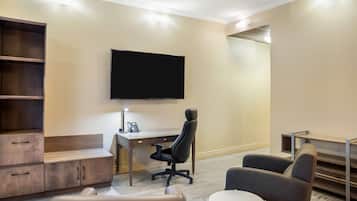 Ett modernt hotellrum med en platt-TV som är monterad på väggen, ett skrivbord med en telefon, en bekväm soffa och ett litet runt bord.