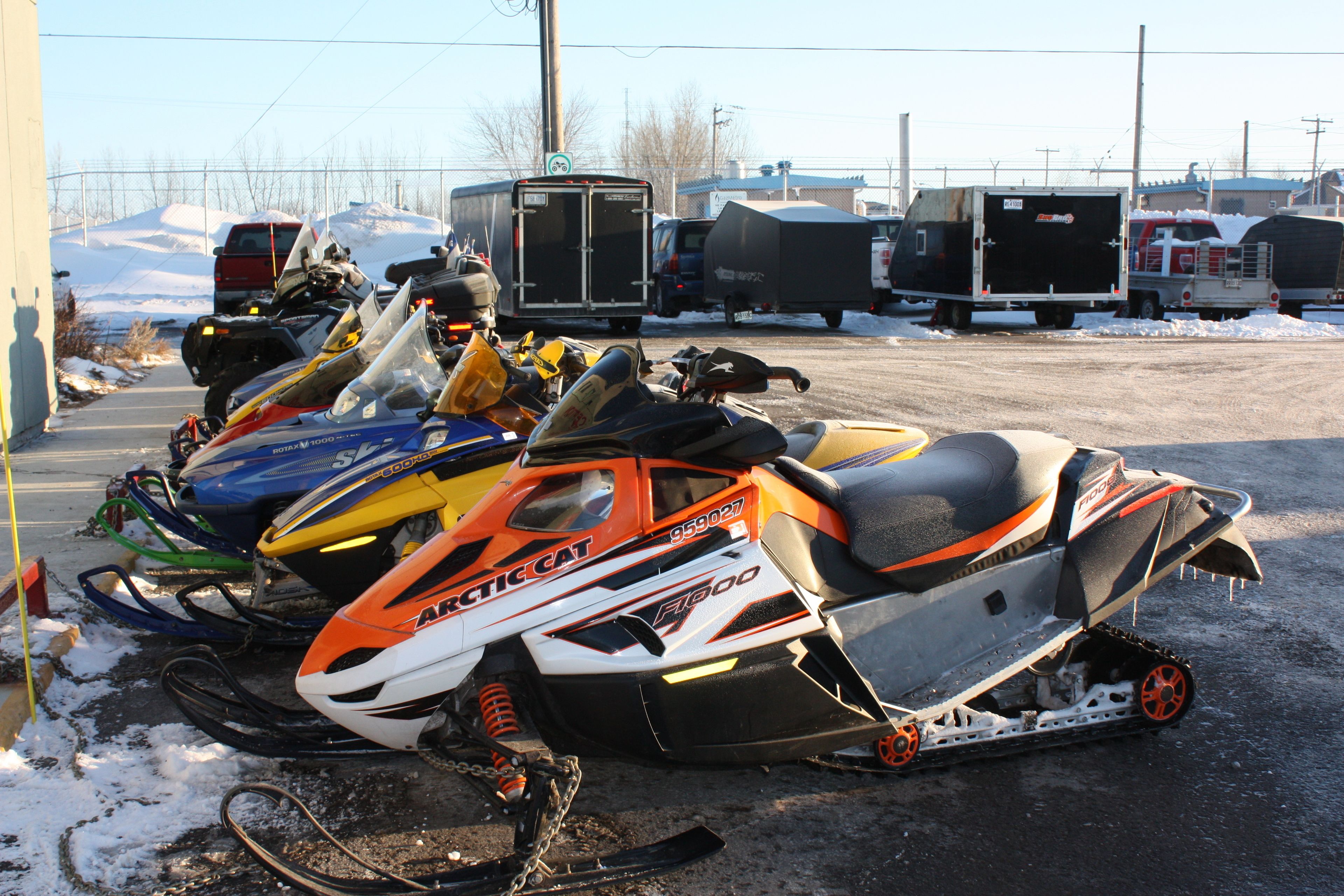 A parking lot with snowmobiles and trailers.