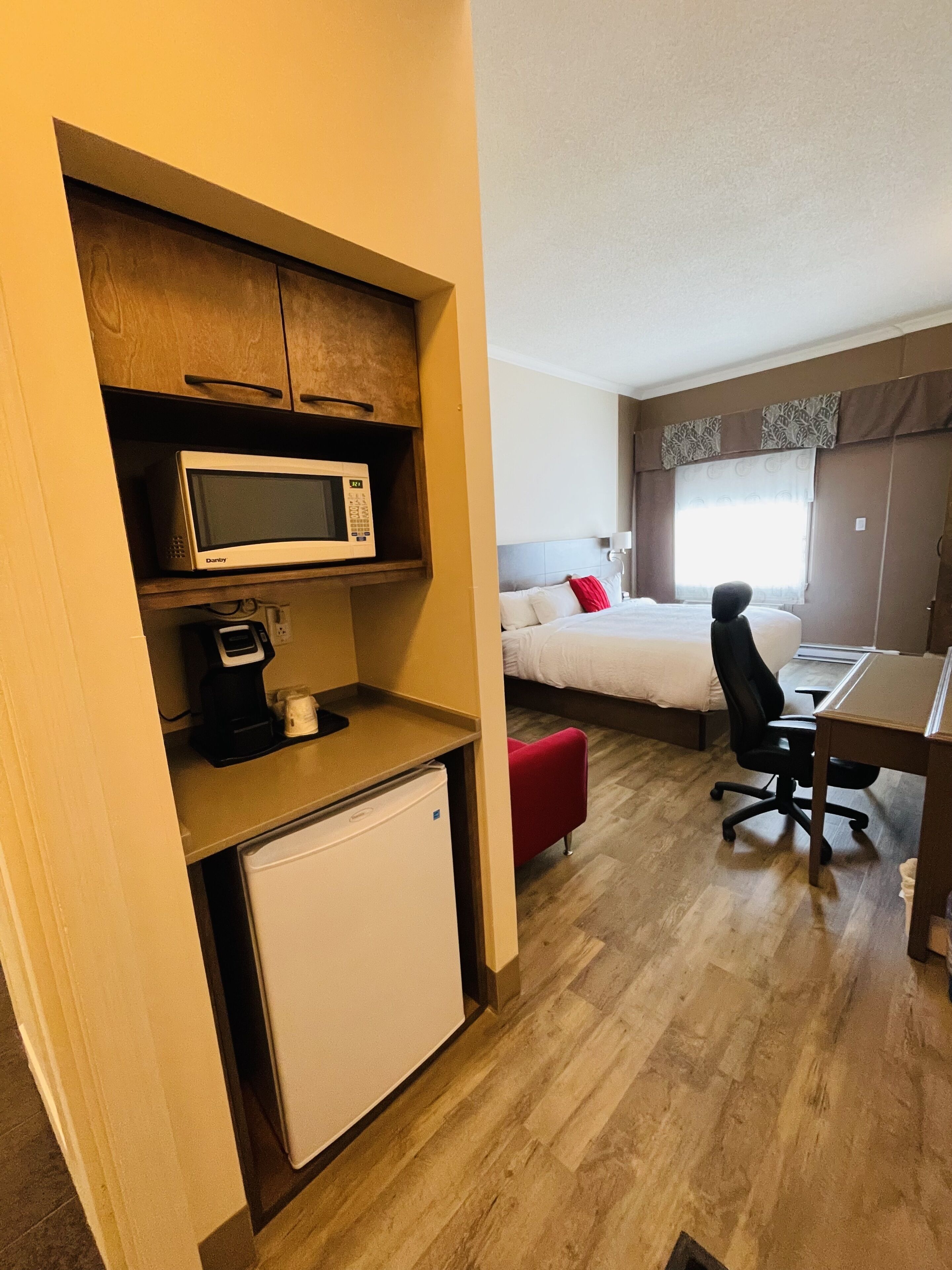 A compact hotel room with a bed, a desk, a chair, a microwave, and a small refrigerator.