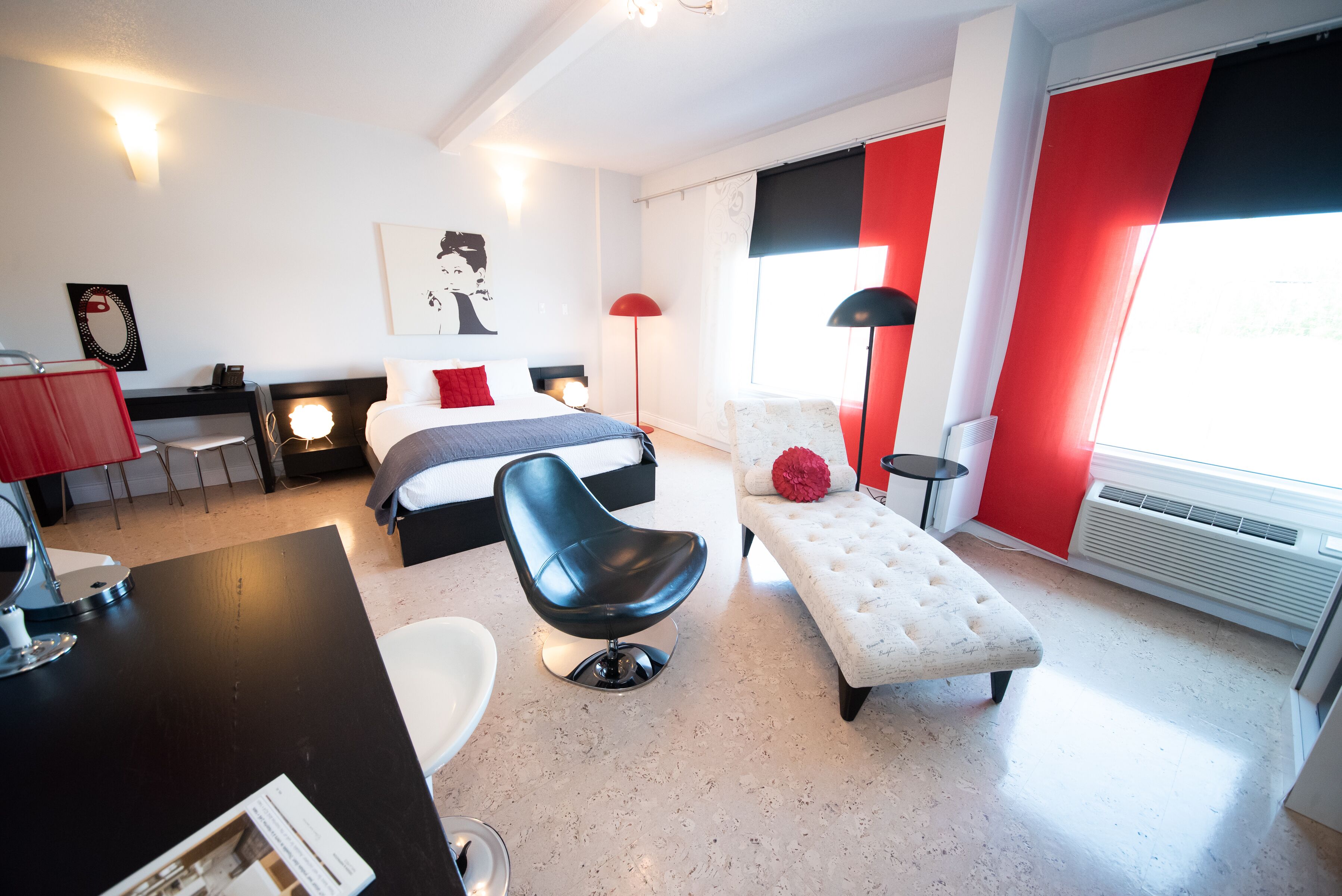 A modern hotel room with a bed, a desk, a chair, and a small sofa.