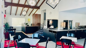 A modern kitchen with a bar area, featuring a coffee machine, refrigerator, and seating area with red chairs and white tables. - Econo Lodge Montreal-Brossard (Brossard)