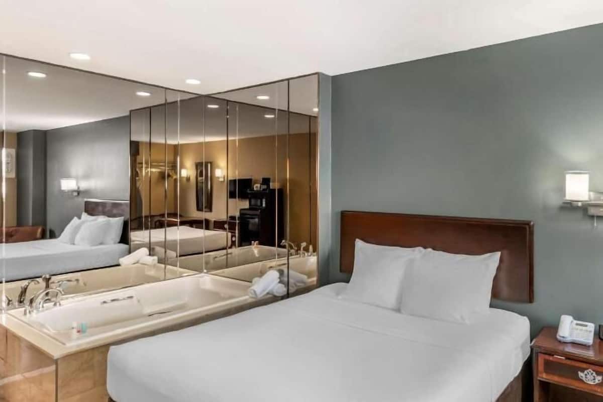 A hotel room with two beds, a large mirror, a bedside table with a phone, and a wall-mounted light fixture.