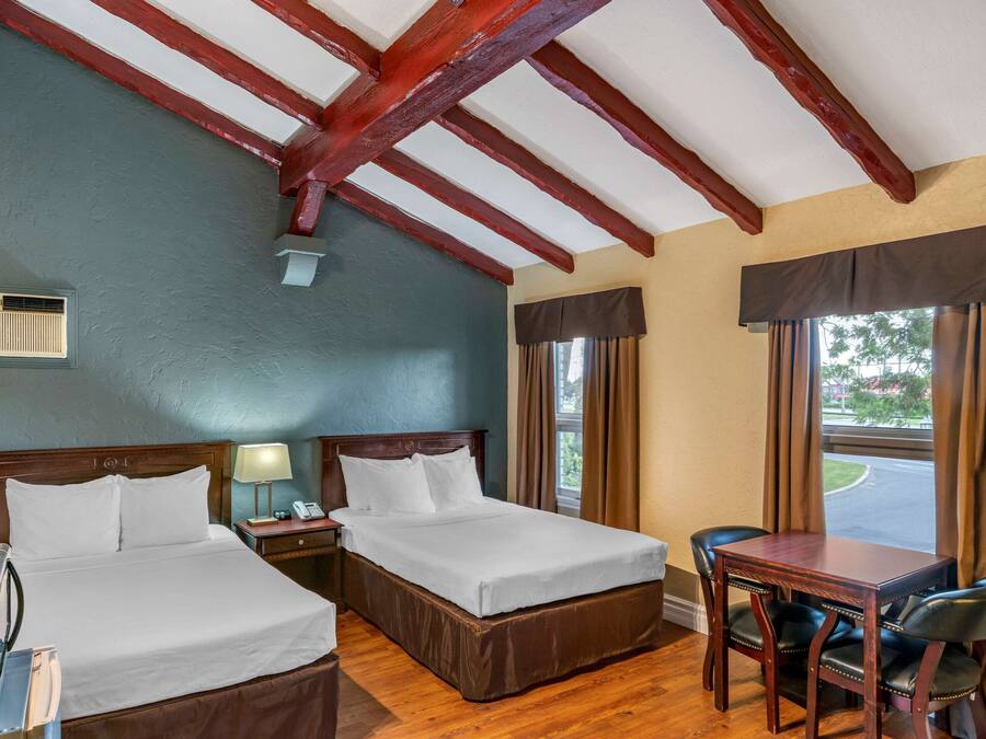 Habitación de hotel con dos camas, un escritorio de madera, una silla, una lámpara, un teléfono y una ventana con cortinas.