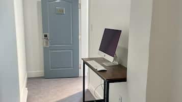 Un pasillo con una puerta azul cerrada, un escritorio con computadora y piso alfombrado.