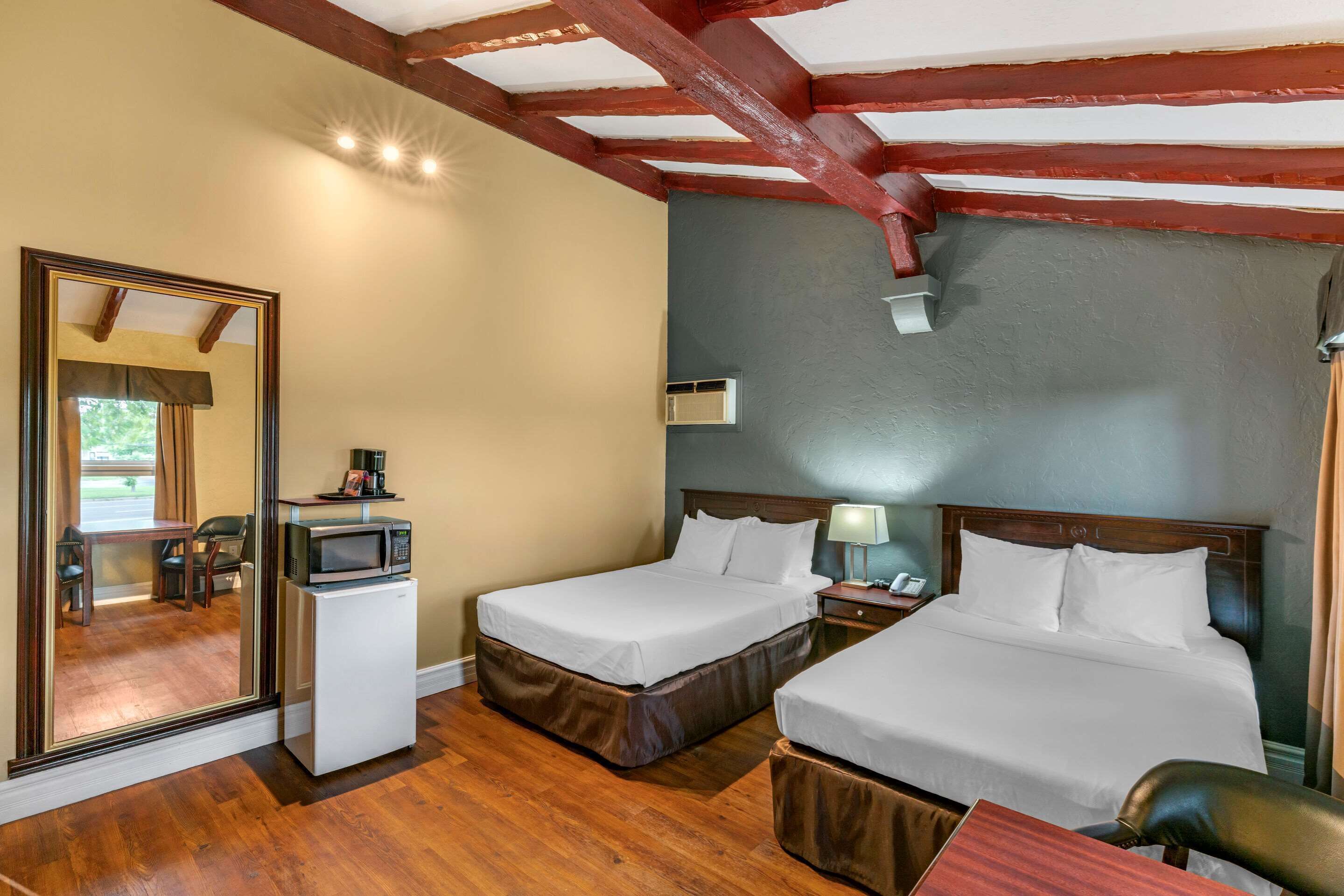 A hotel room with two beds, a small refrigerator, a microwave, a nightstand with a lamp, and a large mirror.