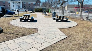 A paved picnic area with benches and tables, surrounded by a fence, with buildings and parked cars in the background. - Econo Lodge Montreal-Brossard (Brossard)
