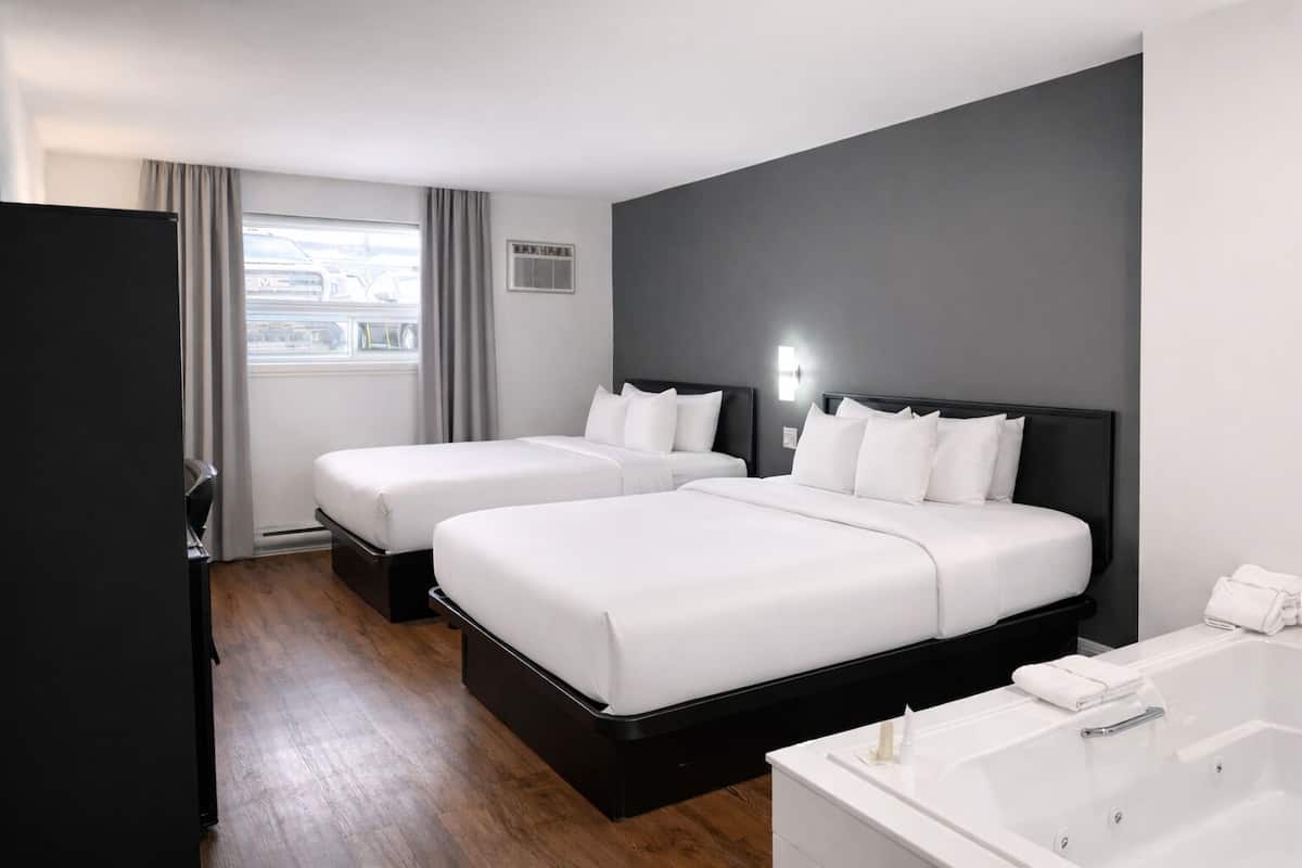 A hotel room with two beds, a bathtub, and a window with curtains.