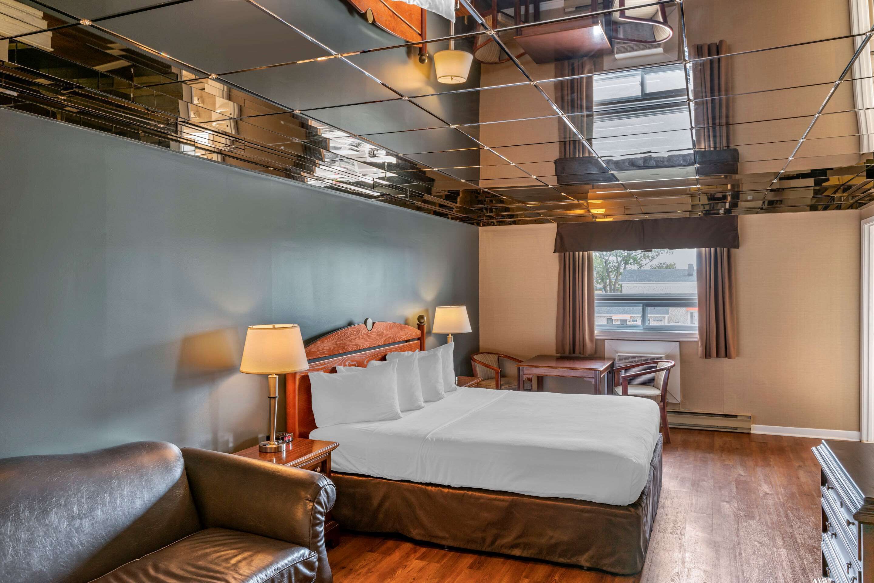 Quarto de hotel moderno com uma cama grande, uma poltrona de couro, uma escrivaninha e vista para a cidade pela janela.