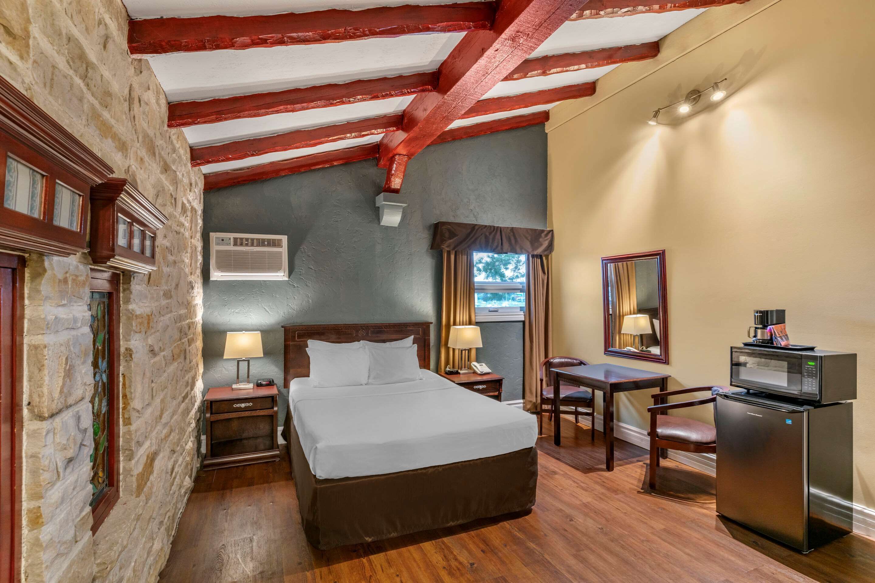 Habitación de hotel con una cama grande, un escritorio, una silla, un refrigerador y una ventana con cortinas.