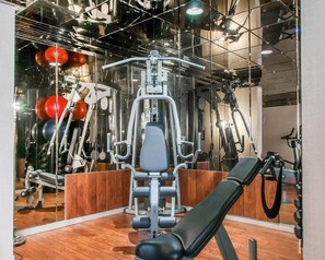 Un gimnasio con equipamiento de ejercicio, una banca y un espejo que refleja el espacio.