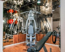 Un gimnasio con equipamiento de ejercicio, una banca y un espejo que refleja el espacio.