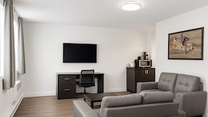 A modern living room with a grey sofa, a flat-screen TV, a desk with a chair, and a cabinet. - Econo Lodge Montreal-Brossard (Brossard)