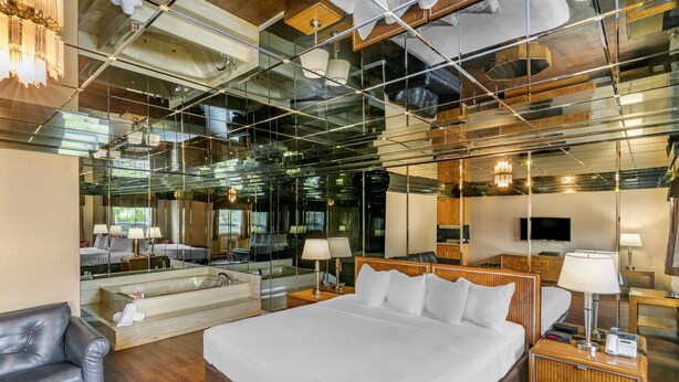 A modern hotel room with a large bed, a sitting area with a sofa, a large mirror, and a television. - Econo Lodge Montreal-Brossard (Brossard)