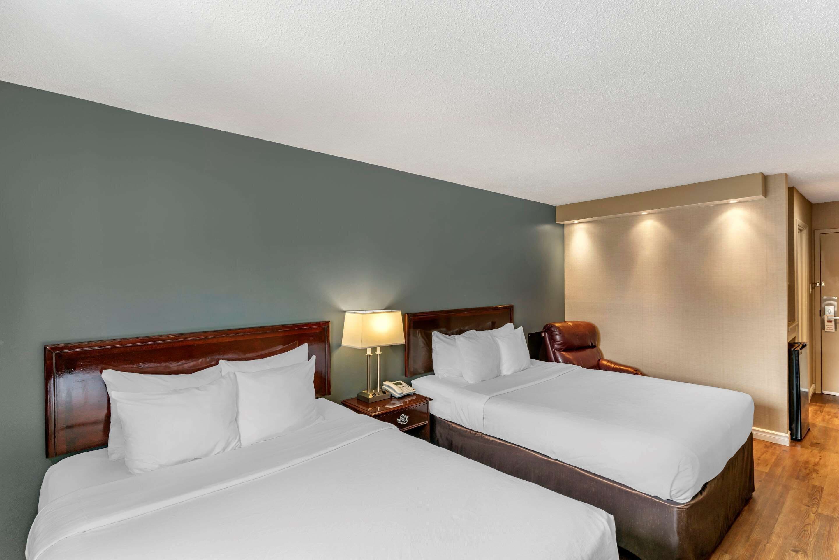A hotel room with two beds, a nightstand with a lamp, and a wooden floor.