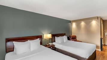 Habitación de hotel con dos camas, una mesita de noche con lámpara y suelo de madera.