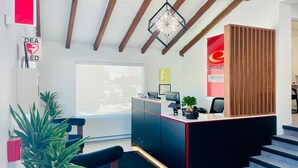 A reception area with a desk, chairs, a potted plant, a fire extinguisher, and a large window. - Econo Lodge Montreal-Brossard (Brossard)