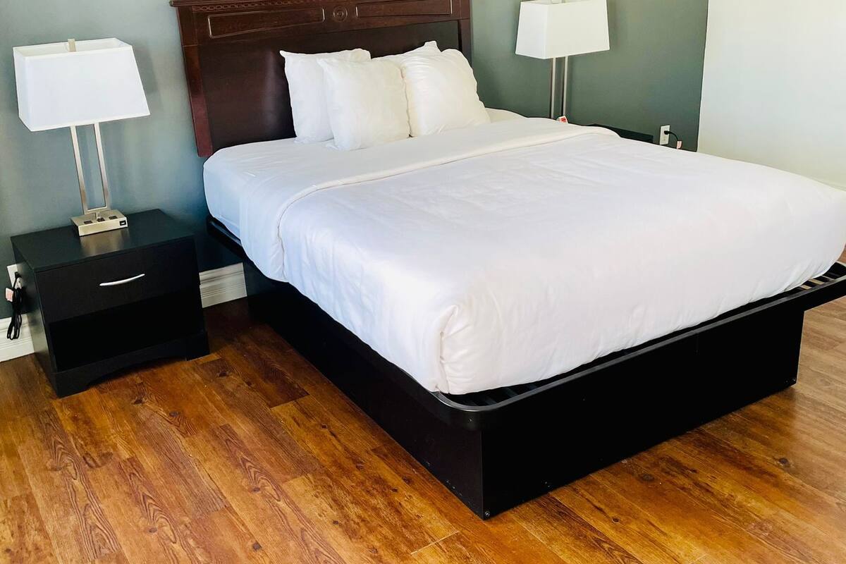 A neatly made bed with white linens in a room with wooden flooring.
