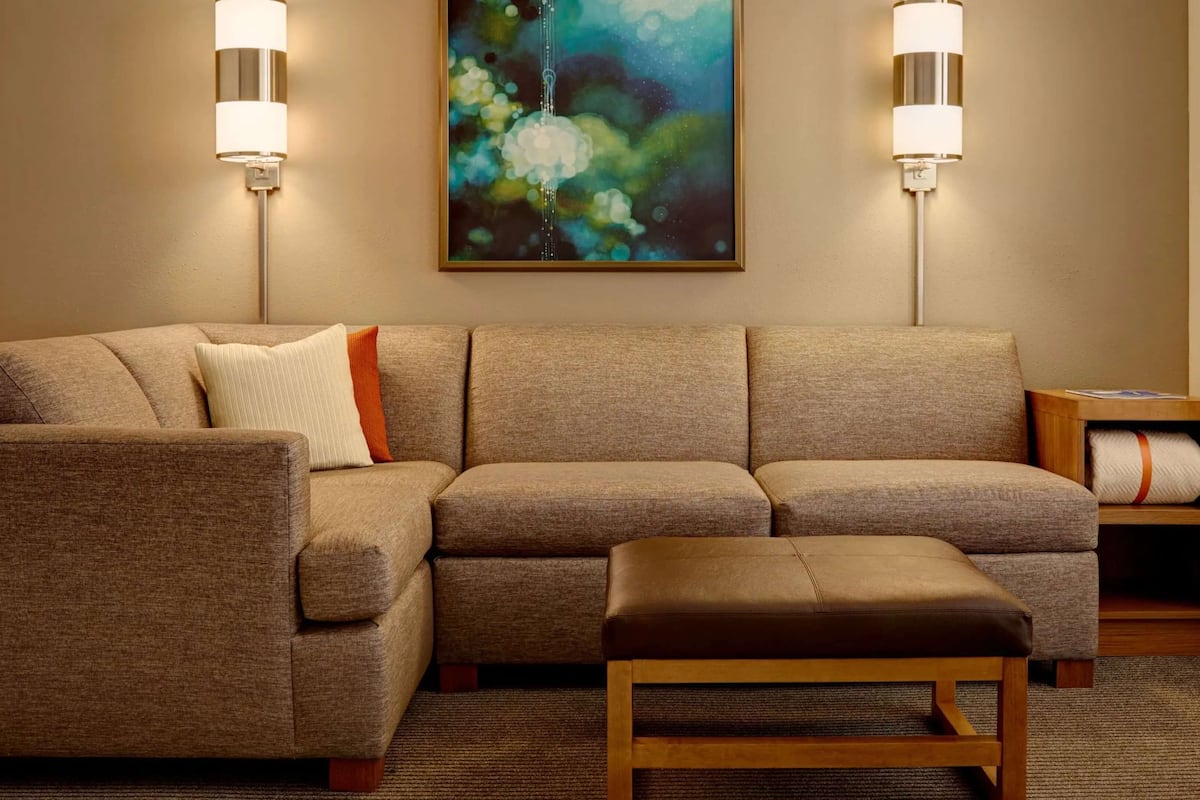 A living room with a sectional sofa, a wooden bench, two wall-mounted lamps, and a painting on the wall.