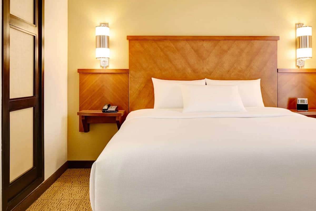A hotel room with a large bed, two bedside tables, a wooden headboard, and two wall-mounted lamps.