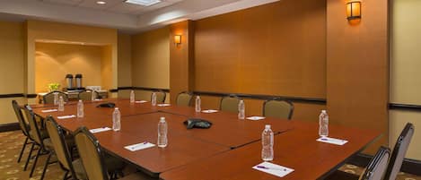 Una sala de conferencias con una mesa larga, sillas, botellas de agua, una estación de café y un teléfono sobre la mesa.