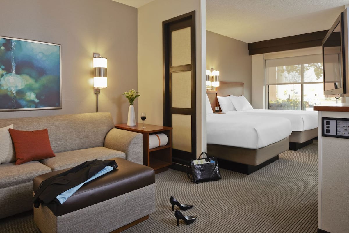 A hotel room with a sofa, a bed, a desk, a mirror, and a painting on the wall.