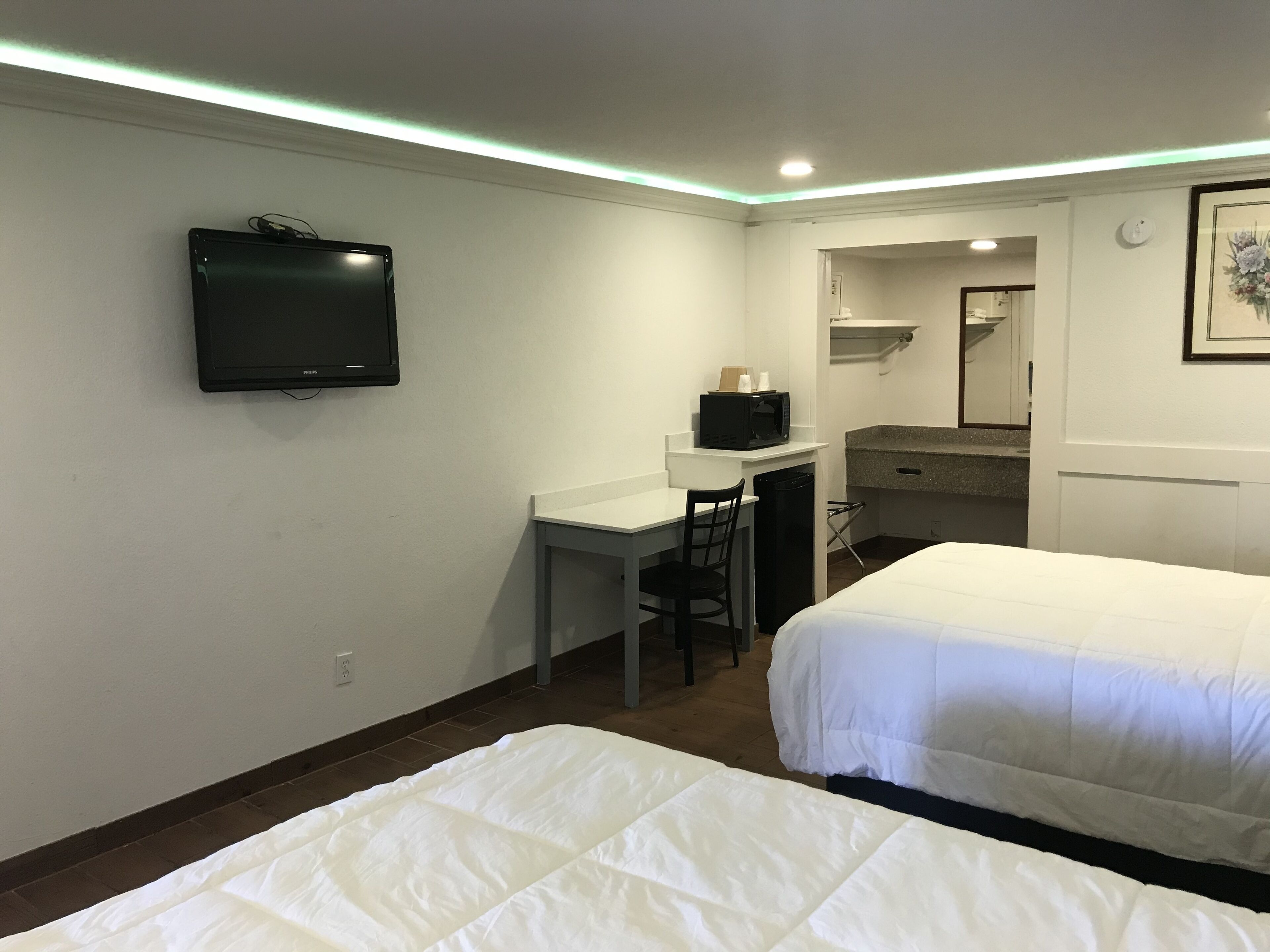 Une chambre d’hôtel avec deux lits, un bureau avec une chaise, un four à micro-ondes et un téléviseur fixé au mur.