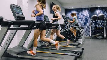 A gym with treadmills lined up against a wall with a patterned mural.