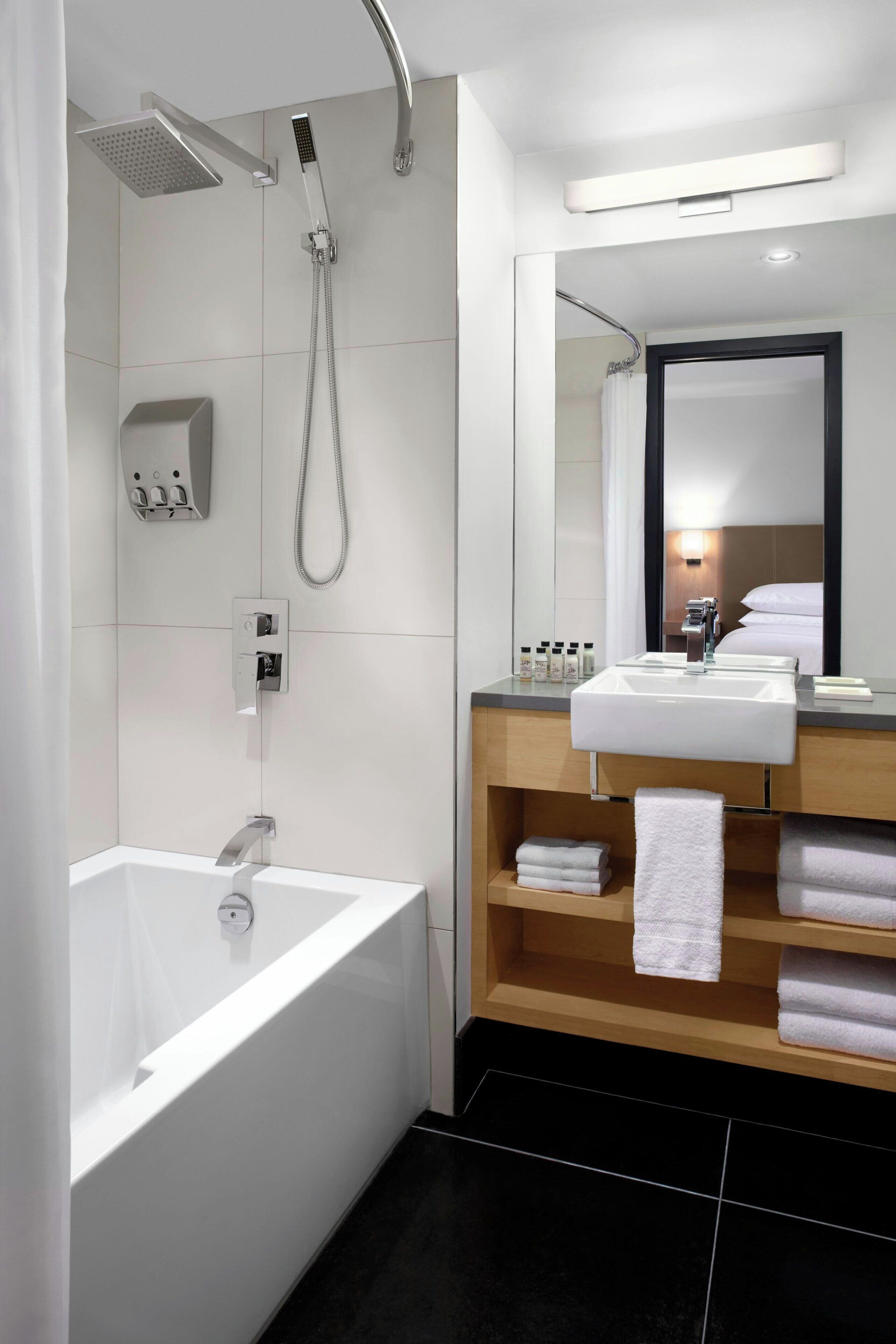 Un baño moderno con bañera, ducha, tocador con lavamanos y espejo.