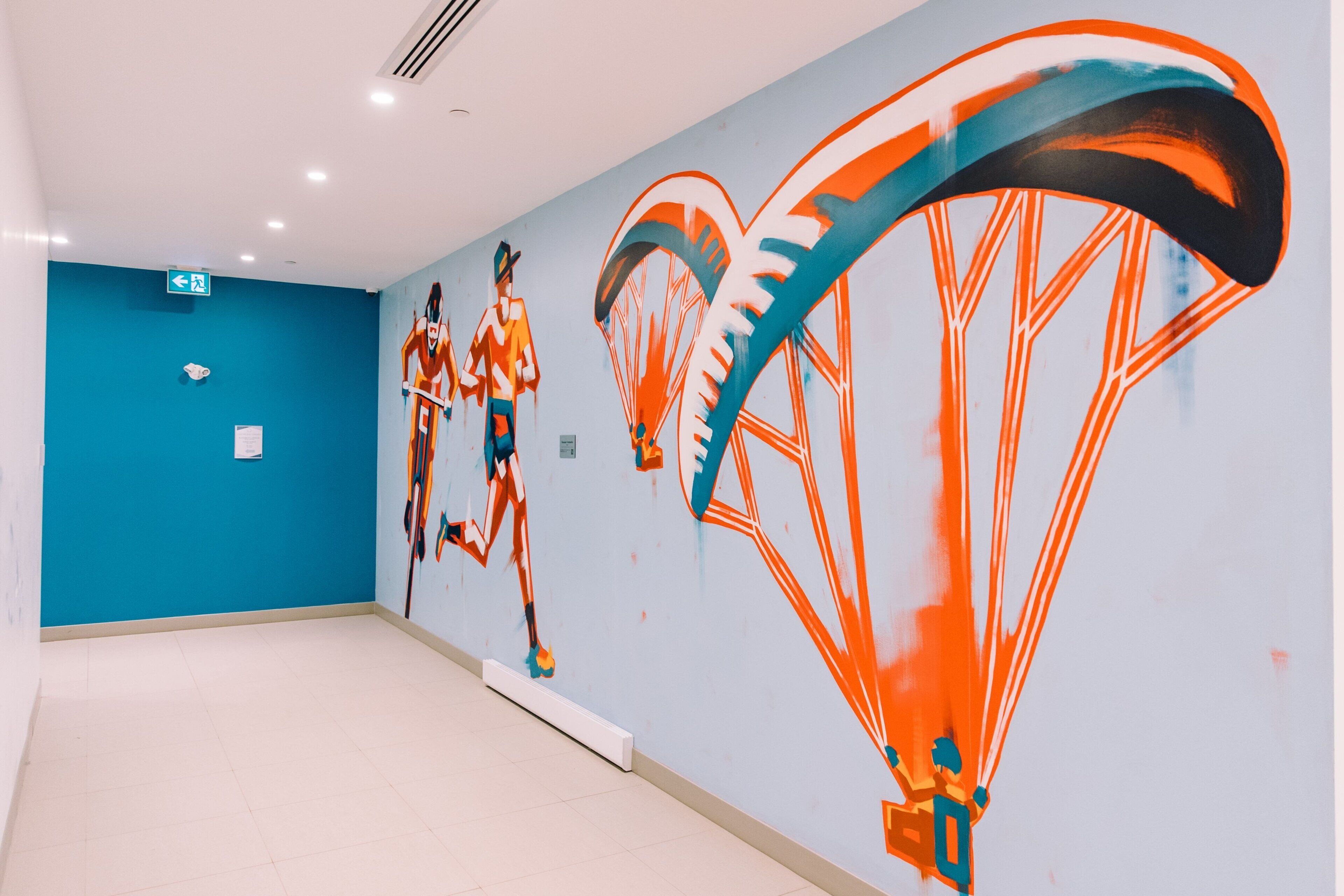 Un pasillo con un mural de una persona en paracaídas, una pared azul y un suelo blanco.